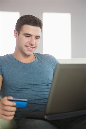 simsearch:400-07474252,k - Smiling handsome man relaxing on couch using laptop shopping online in bright living room Stock Photo - Budget Royalty-Free & Subscription, Code: 400-07138459