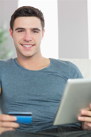 simsearch:400-07474252,k - Cheerful handsome man relaxing on couch using tablet shopping online in bright living room Stock Photo - Budget Royalty-Free & Subscription, Code: 400-07138453