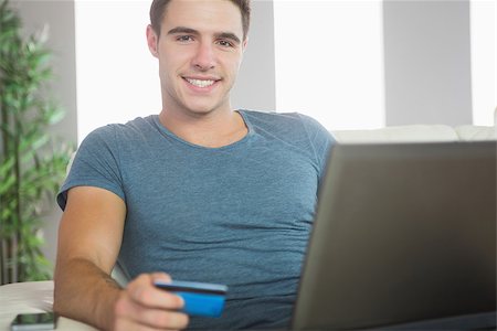 simsearch:400-07474252,k - Cheerful handsome man relaxing on couch using laptop shopping online in bright living room Stock Photo - Budget Royalty-Free & Subscription, Code: 400-07138460