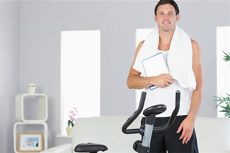 Smiling sporty man standing behind exercise bike holding tablet in bright living room Stock Photo - Budget Royalty-Free & Subscription, Code: 400-07138971