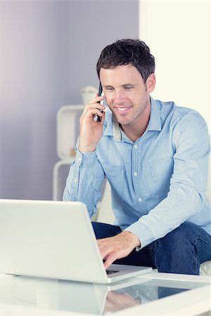 Smiling casual man using laptop and phoning in bright living room Stock Photo - Budget Royalty-Free & Subscription, Code: 400-07139027