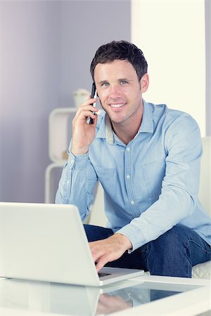 Cheerful casual man using laptop and phoning in bright living room Stock Photo - Budget Royalty-Free & Subscription, Code: 400-07139028