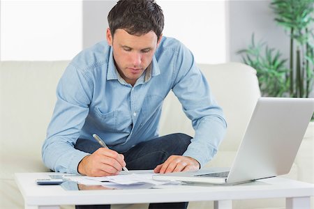 simsearch:400-07333928,k - Serious casual man writing on sheets paying bills in bright living room Stock Photo - Budget Royalty-Free & Subscription, Code: 400-07139097