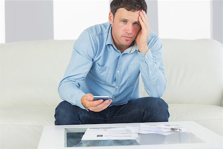 simsearch:400-07333928,k - Upset casual man using calculator and looking at camera paying bills in bright living room Stock Photo - Budget Royalty-Free & Subscription, Code: 400-07139090