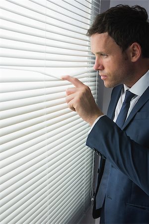 simsearch:400-07139155,k - Stern handsome businessman looking through roller blind in dark room Stock Photo - Budget Royalty-Free & Subscription, Code: 400-07139144