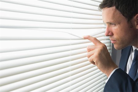 Serious handsome businessman looking through roller blind in dark room Stock Photo - Budget Royalty-Free & Subscription, Code: 400-07139145