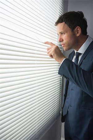 Unsmiling handsome businessman looking through roller blind in dark room Stock Photo - Budget Royalty-Free & Subscription, Code: 400-07139146