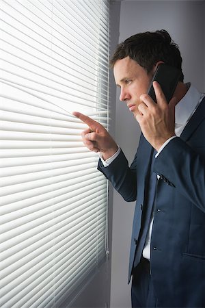 Stern handsome businessman looking through roller blind phoning in dark room Stock Photo - Budget Royalty-Free & Subscription, Code: 400-07139148