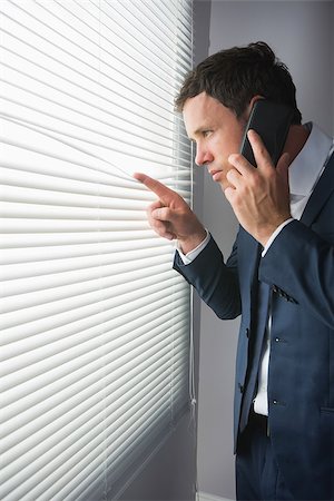 Serious handsome businessman looking through roller blind phoning in dark room Stock Photo - Budget Royalty-Free & Subscription, Code: 400-07139149