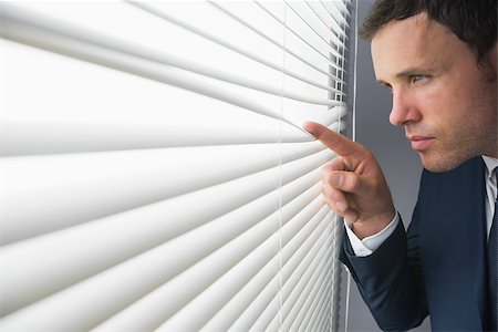 simsearch:400-07139155,k - Stern attractive businessman spying through roller blind in dark room Stock Photo - Budget Royalty-Free & Subscription, Code: 400-07139150