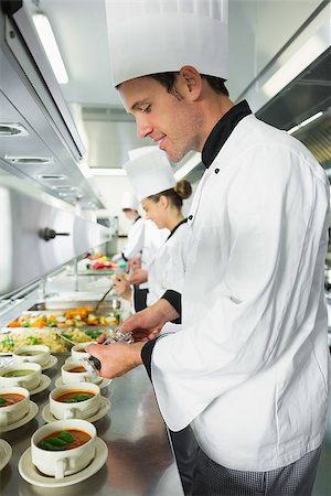 restaurant work teenager - Smiling handsome chef seasoning his soup standing in the kitchen Photographie de stock - Aubaine LD & Abonnement, Code: 400-07139971