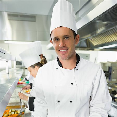 simsearch:400-07140008,k - Handsome male chef posing in the kitchen smiling at the camera Photographie de stock - Aubaine LD & Abonnement, Code: 400-07139973
