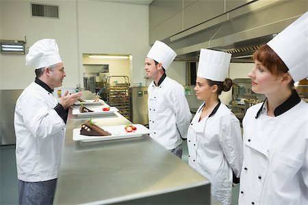 simsearch:400-07140008,k - Three chefs presenting their dessert plates to the head chef in busy kitchen Photographie de stock - Aubaine LD & Abonnement, Code: 400-07139986