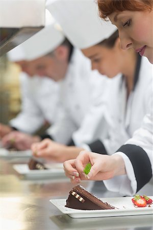 simsearch:400-07140008,k - Team of young chefs in a row garnishing dessert plates in commercial kitchen Photographie de stock - Aubaine LD & Abonnement, Code: 400-07139980