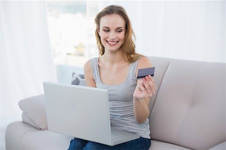 simsearch:400-07474252,k - Cheerful young woman sitting on couch using laptop for online shopping at home in the living room Stock Photo - Budget Royalty-Free & Subscription, Code: 400-07130025