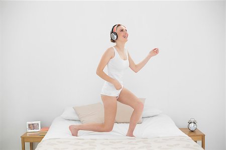 Laughing woman playing air guitar while listening to music and standing on her bed Stock Photo - Budget Royalty-Free & Subscription, Code: 400-07131105