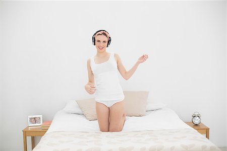 Woman playing air guitar while listening to music, kneeling on her bed and looking into the camera Stock Photo - Budget Royalty-Free & Subscription, Code: 400-07131103