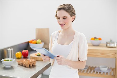 Smiling cute woman using her tablet standing in her kitchen at home Stock Photo - Budget Royalty-Free & Subscription, Code: 400-07131234