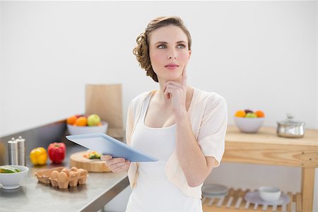 Thoughtful beautiful woman holding her tablet while standing in her kitchen at home Stock Photo - Budget Royalty-Free & Subscription, Code: 400-07131237