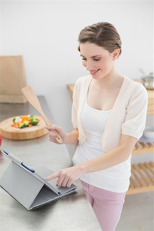 Smiling brunette woman using her tablet while standing in her kitchen at home Stock Photo - Budget Royalty-Free & Subscription, Code: 400-07131305