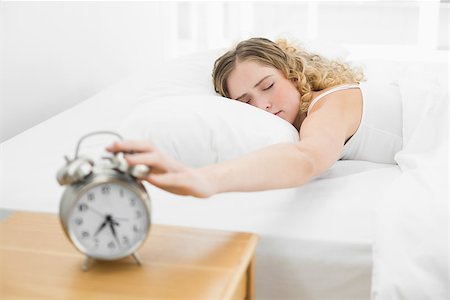 Pretty tired blonde lying in bed turning off alarm clock in bright bedroom Photographie de stock - Aubaine LD & Abonnement, Code: 400-07132421