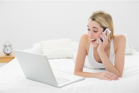 shocked teen computer - Astonished lovely woman phoning with her smartphone looking at her laptop lying on her bed Stock Photo - Budget Royalty-Free & Subscription, Code: 400-07132717