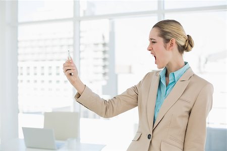 Attractive young businesswoman looking shocked at her smartphone standing in her office Stock Photo - Budget Royalty-Free & Subscription, Code: 400-07132882