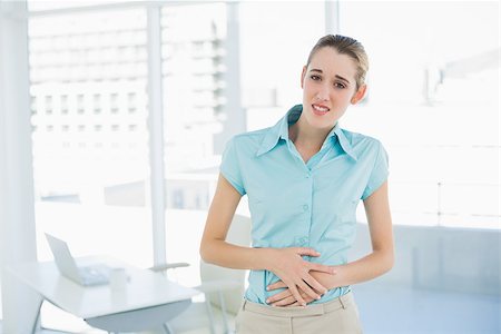 Gorgeous young businesswoman holding her aching belly looking at camera Stock Photo - Budget Royalty-Free & Subscription, Code: 400-07132909