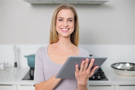 Smiling gorgeous model using tablet looking at camera standing in kitchen Stock Photo - Budget Royalty-Free & Subscription, Code: 400-07133120