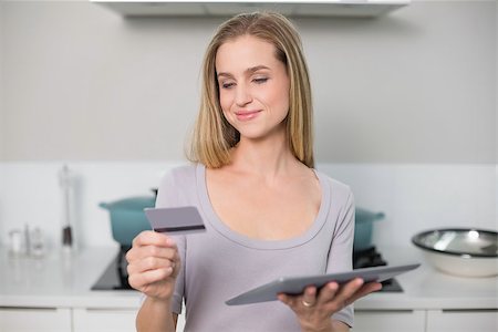 Smiling gorgeous model holding tablet and credit card standing in kitchen Stock Photo - Budget Royalty-Free & Subscription, Code: 400-07133121