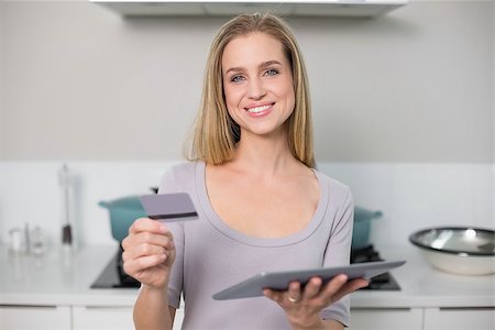 Cheerful gorgeous model holding tablet and credit card standing in kitchen Stock Photo - Budget Royalty-Free & Subscription, Code: 400-07133122