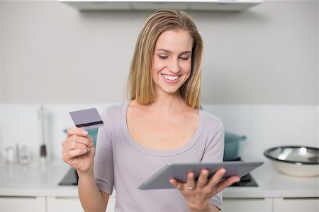 Happy gorgeous model holding tablet and credit card standing in kitchen Stock Photo - Budget Royalty-Free & Subscription, Code: 400-07133123