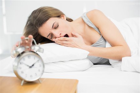 Tired brunette woman turning off the alarm clock while yawning lying on her bed Photographie de stock - Aubaine LD & Abonnement, Code: 400-07133552