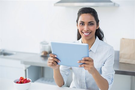 Lovely young woman holding her tablet standing in bright kitchen smiling at camera Stock Photo - Budget Royalty-Free & Subscription, Code: 400-07133940