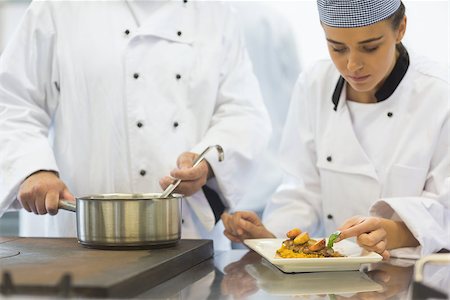 simsearch:400-07140008,k - Young female chef finishing a plate next to her colleague in kitchen Photographie de stock - Aubaine LD & Abonnement, Code: 400-07140020