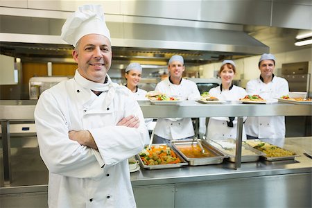 simsearch:400-07140055,k - Proud mature head chef posing in a modern kitchen with his colleagues in the background Stock Photo - Budget Royalty-Free & Subscription, Code: 400-07140047