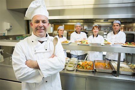 simsearch:400-07140055,k - Experienced head chef posing proudly in a modern kitchen with his team in the background Stock Photo - Budget Royalty-Free & Subscription, Code: 400-07140048