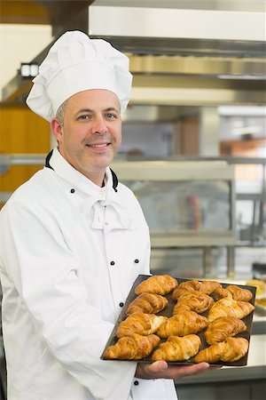 simsearch:400-07140099,k - Baker showing some croissants on a baking tray smiling at the camera Foto de stock - Royalty-Free Super Valor e Assinatura, Número: 400-07140079