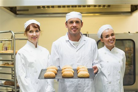 simsearch:400-07140055,k - Young male baker holding a baking tray with rolls on it posing with colleagues Stock Photo - Budget Royalty-Free & Subscription, Code: 400-07140094