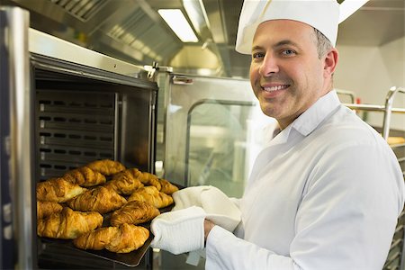 simsearch:400-07140099,k - Mature baker smiling proudly at the camera take some croissants out of oven Foto de stock - Royalty-Free Super Valor e Assinatura, Número: 400-07140092