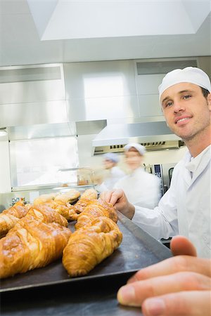 simsearch:400-07140099,k - Young male baker standing in a bakery in front of a baking tray with croissants Foto de stock - Royalty-Free Super Valor e Assinatura, Número: 400-07140107