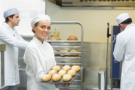 Cute young female baker holding a baking tray with rolls on it smiling at the camera Stock Photo - Budget Royalty-Free & Subscription, Code: 400-07140100