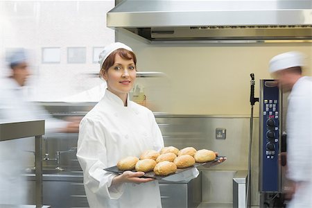 simsearch:400-07140099,k - Cute female baker holding a baking tray with rolls on it smiling at the camera Foto de stock - Royalty-Free Super Valor e Assinatura, Número: 400-07140101