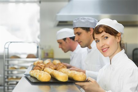 Happy female baker smiling at the camera while holding a baking tray Stock Photo - Budget Royalty-Free & Subscription, Code: 400-07140103