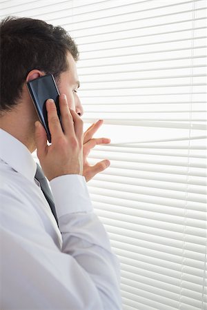Attractive businessman spying through roller blind while phoning in bright office Stock Photo - Budget Royalty-Free & Subscription, Code: 400-07141029