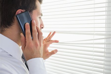 Handsome businessman spying through roller blind while phoning in bright office Stock Photo - Budget Royalty-Free & Subscription, Code: 400-07141030