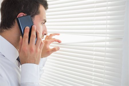 Serious businessman spying through roller blind while phoning in bright office Stock Photo - Budget Royalty-Free & Subscription, Code: 400-07141031