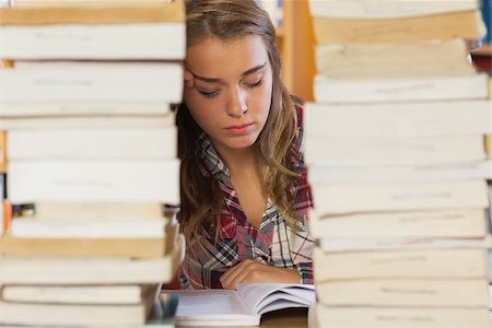 simsearch:6109-07497515,k - Concentrated pretty student studying between piles of books in library Photographie de stock - Aubaine LD & Abonnement, Code: 400-07141917