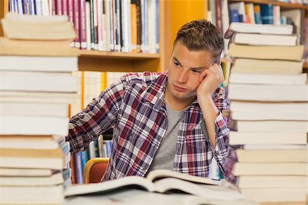 simsearch:400-07141917,k - Frustrated handsome student studying between piles of books in library Stock Photo - Budget Royalty-Free & Subscription, Code: 400-07141924