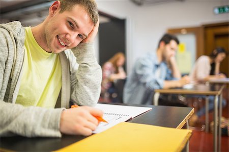 simsearch:400-07180633,k - Portrait of a smiling male student with others writing notes in the classroom Foto de stock - Super Valor sin royalties y Suscripción, Código: 400-07142405